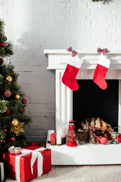 Christmas tree with baubles, gift boxes and fireplace with christmas stockings at home — Stock Photo