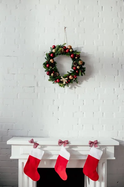 Camino con calze di Natale e ghirlanda di abete con le bagattelle appese al muro di mattoni in camera — Foto stock