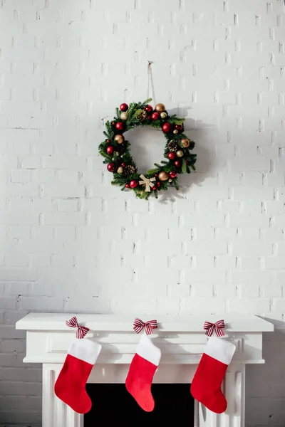 Fireplace with christmas stockings and fir wreath with baubles hanging on brick wall in room — Stock Photo