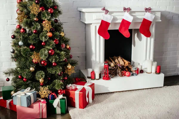 Christmas tree with baubles, gift boxes and fireplace with christmas stockings in room — Stock Photo