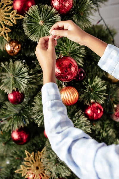 Zugeschnittenes Bild eines afrikanisch-amerikanischen Kindes im Pyjama, das zu Hause den Weihnachtsbaum mit Christbaumkugeln schmückt — Stockfoto