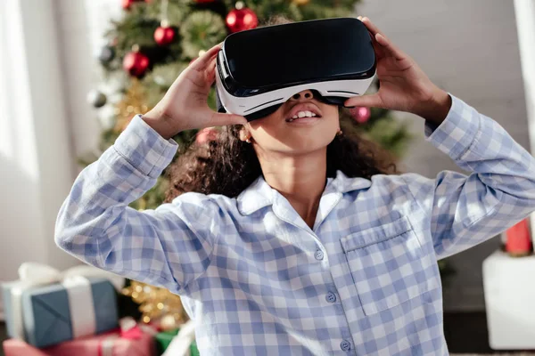 African american child in pajamas using virtual reality headset at home, christmas concept — Stock Photo