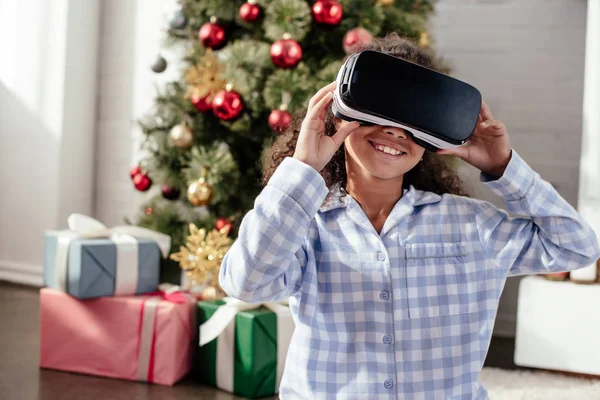 Happy african american child in pajamas using virtual reality headset at home, christmas concept — Stock Photo