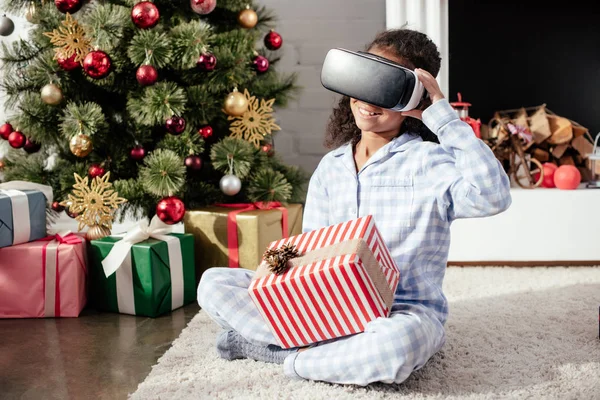 Smiling african american child in pajamas using virtual reality headset at home, christmas concept — Stock Photo
