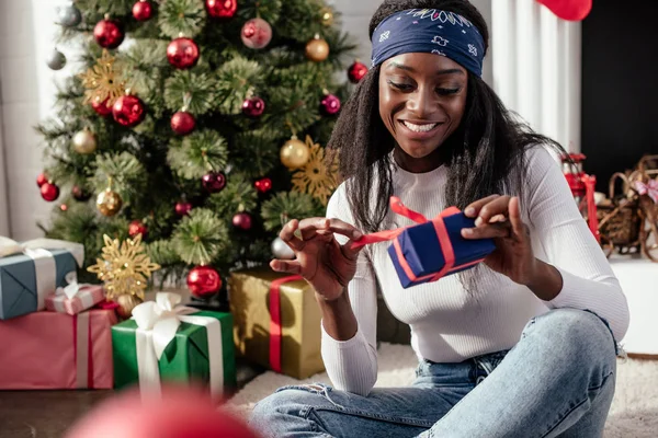 Glücklich attraktive afrikanisch-amerikanische Frau eröffnet Weihnachtsgeschenk zu Hause — Stockfoto