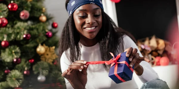 Smiling attractive african american woman opening christmas present at home — Stock Photo