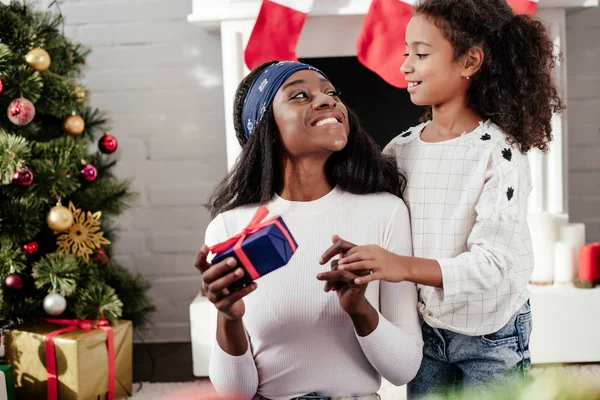 Africana americana hija regalando navidad presente a la madre en casa - foto de stock