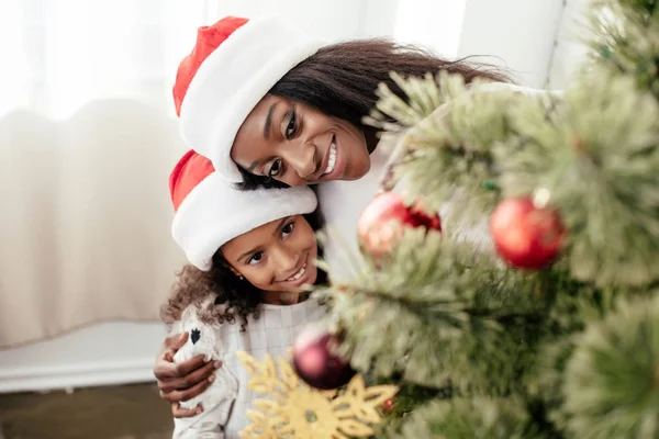 Glückliche afrikanisch-amerikanische Familie in Weihnachtsmannhüten, die zu Hause gemeinsam den Weihnachtsbaum schmücken — Stockfoto