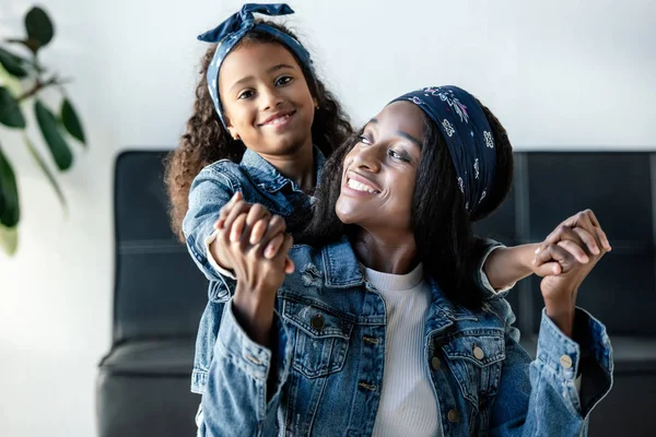 Süße afrikanisch-amerikanische Kind umarmt lächelnde Mutter in ähnlicher Kleidung zu Hause — Stockfoto