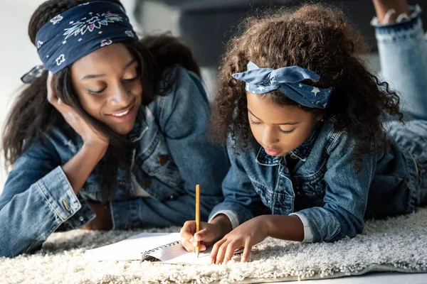 Portrait of african american woman helping daughter doing homework at home — Stock Photo