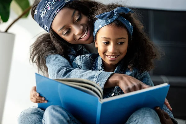 Portrait of african american mother and daughter looking at family photo album at home — Stock Photo