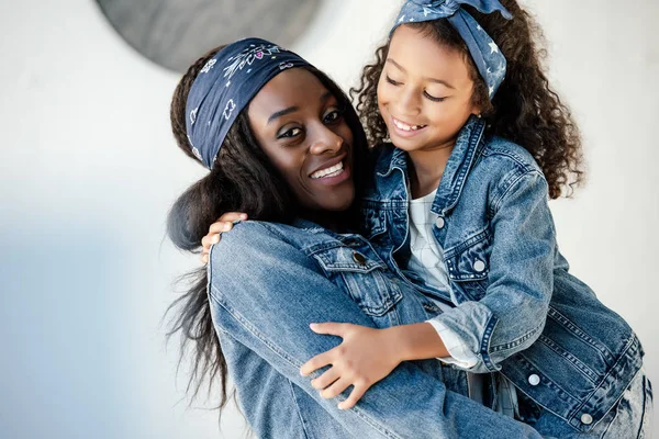 Happy african american woman holding little daughter in similar clothing on hands at home — Stock Photo