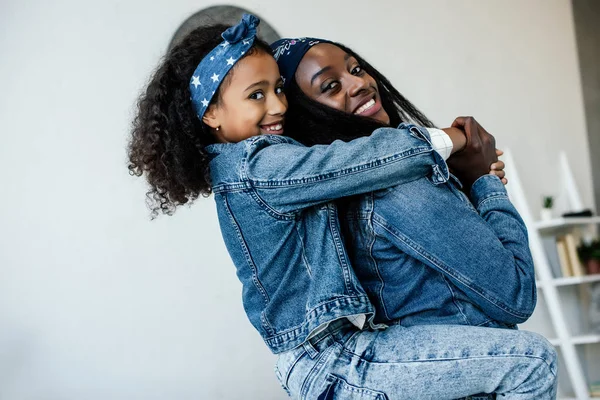 Cute african american kid hugging smiling mother in similar clothing at home — Stock Photo