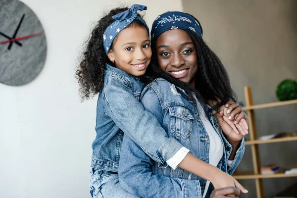 Süße afrikanisch-amerikanische Kind umarmt lächelnde Mutter in ähnlicher Kleidung zu Hause — Stockfoto