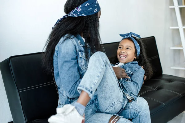 Africana americana mujer y alegre hija tener divertido en sofá en casa - foto de stock