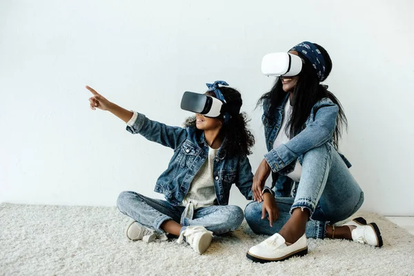 African american mother and daughter in similar clothing and vr headsets at home — Stock Photo