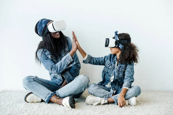 African american mother and daughter in similar clothing and vr headsets giving high five to each other at home — Stock Photo