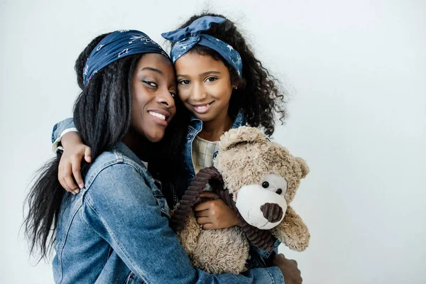 Portrait of smiling african american daughter with teddy bear hugging mother at home — Stock Photo