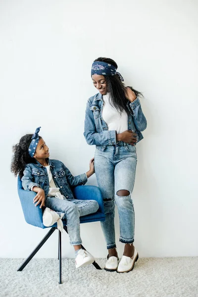 Sorridente madre afro-americana in piedi vicino a figlia sulla sedia a casa — Foto stock