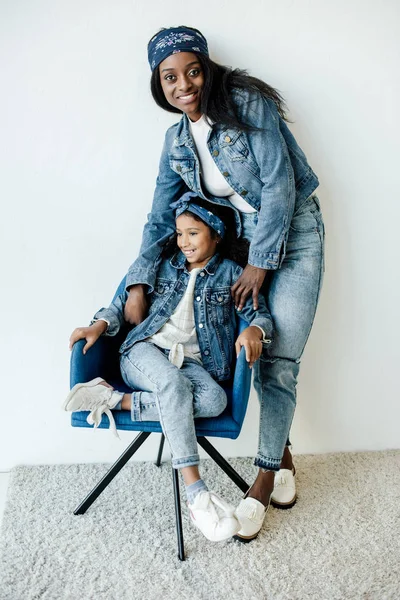 Lächelnde afrikanisch-amerikanische Mutter neben Tochter auf Stuhl zu Hause — Stockfoto