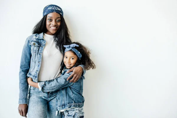 Portrait de la mère et la fille afro-américaine élégante dans des vêtements similaires posant au mur à la maison — Photo de stock