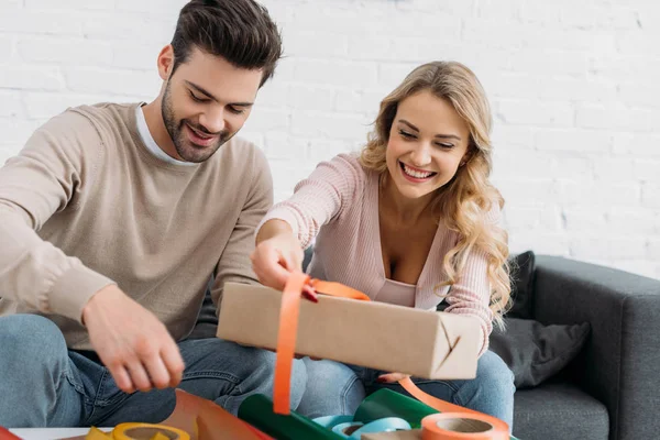 Couple souriant préparant boîte cadeau de Noël ensemble à la maison — Photo de stock