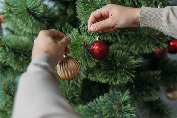 Abgeschnittenes Bild eines Mannes, der zu Hause Weihnachtsbaum mit Christbaumkugeln schmückt — Stockfoto