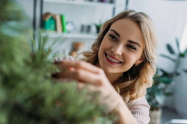 Smiling attractive girl decorating christmas tree with baubles at home — Stock Photo