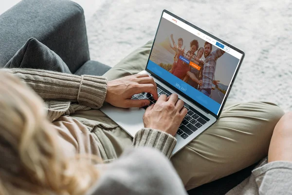 Recortado disparo de pareja utilizando el ordenador portátil con couchsurfing sitio web en la pantalla en el sofá en casa - foto de stock