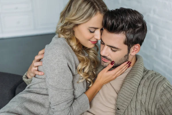 Joven sonriente abrazando a su novio en el sofá en casa - foto de stock