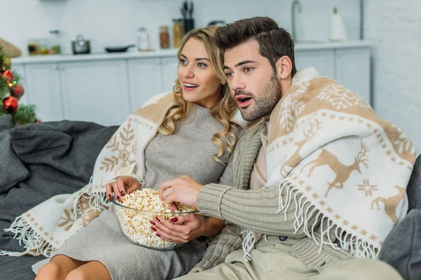 Excitada pareja joven con palomitas de maíz viendo películas en casa - foto de stock