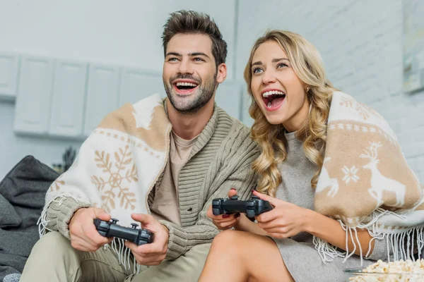 Hermosa pareja joven jugando videojuegos y divertirse juntos en el sofá en casa - foto de stock