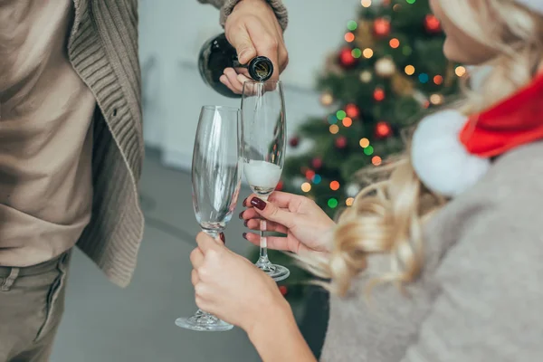 Cropped shot of couple pouring champagne into glasses in front of christmas tree at home — Stock Photo