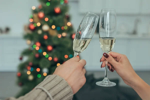 Colpo ritagliato di coppia bicchieri tintinnanti di champagne a Natale a casa — Foto stock