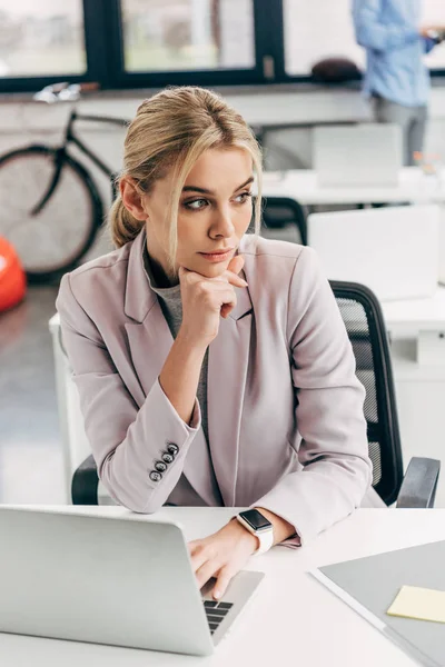 Pensive young businesswoman looking away while working with laptop in office — Stock Photo