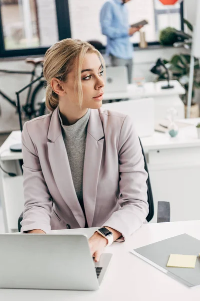 Giovane donna d'affari che distoglie lo sguardo mentre lavora con il laptop in ufficio — Foto stock