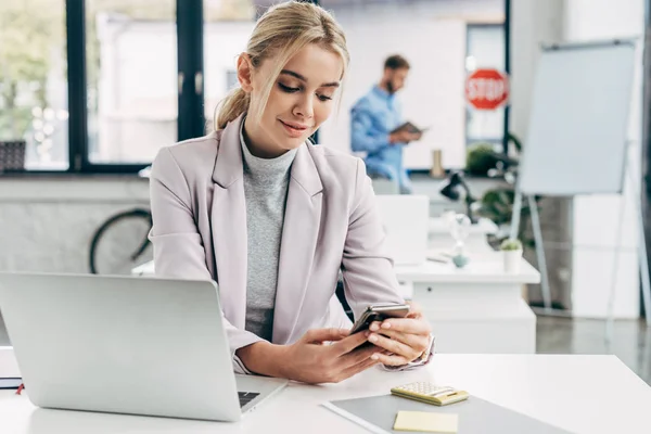 Sorridente jovem empresária usando smartphone no local de trabalho — Fotografia de Stock