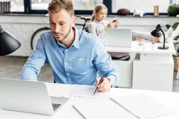 Jeune homme d'affaires utilisant un ordinateur portable et travaillant avec contrat dans le bureau — Photo de stock