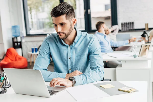 Красивий бородатий молодий бізнесмен використовує ноутбук на робочому місці — стокове фото