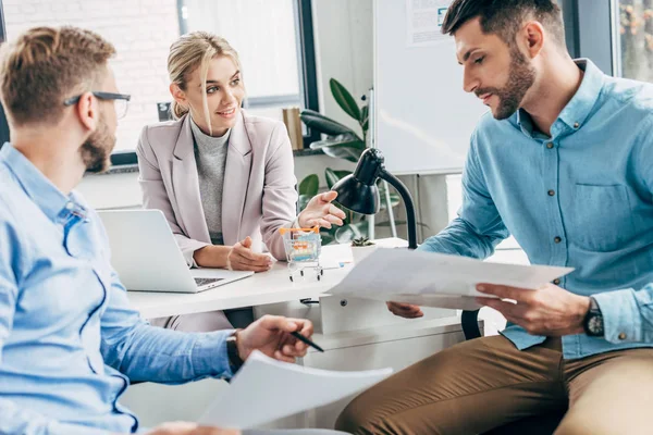 Equipo joven de start up sosteniendo papeles y discutiendo cartas de negocios en la oficina - foto de stock