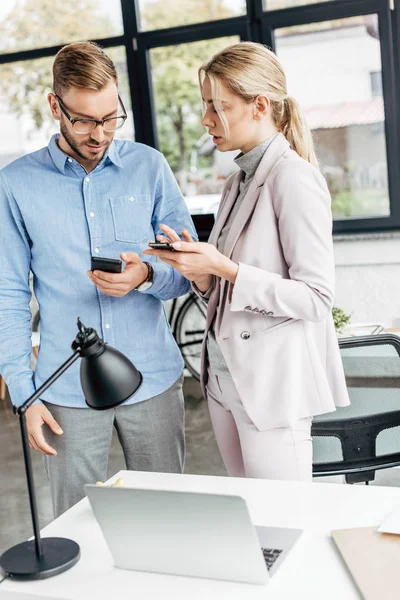 Joven hombre de negocios y mujer de negocios utilizando teléfonos inteligentes juntos en la oficina - foto de stock