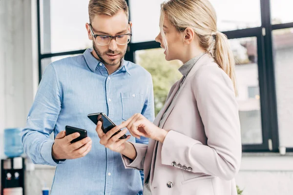 Jeunes collègues d'affaires utilisant des smartphones et parlant sur le lieu de travail — Photo de stock