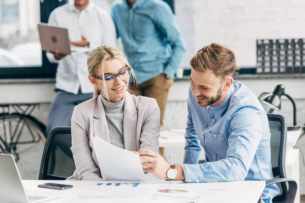 Lächelnde junge Geschäftskollegen, die mit Papieren im Büro arbeiten — Stockfoto