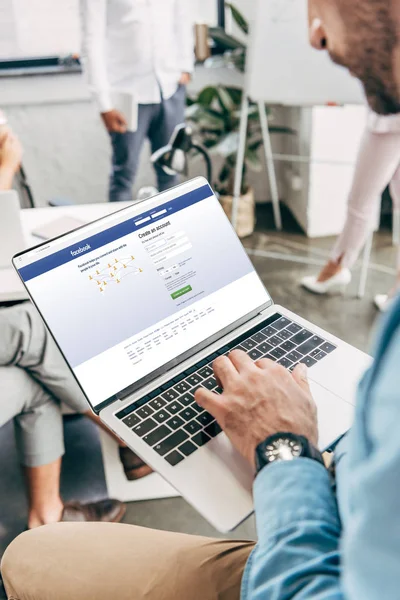 Cropped shot of young businessman using laptop with facebook website on screen — Stock Photo