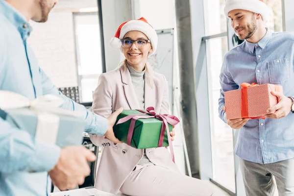 Улыбающиеся молодые коллеги вручают рождественские подарки в офисе — стоковое фото