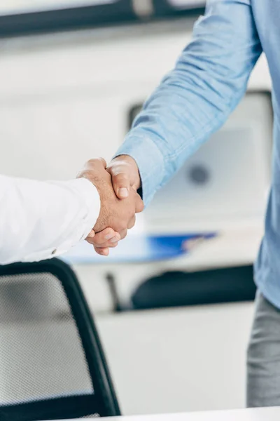 Close-up partial view of businessmen shaking hands at workplace — Stock Photo