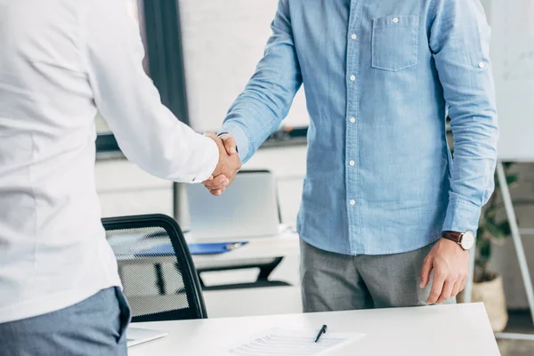 Recortado tiro de hombres de negocios estrechando la mano en el lugar de trabajo - foto de stock