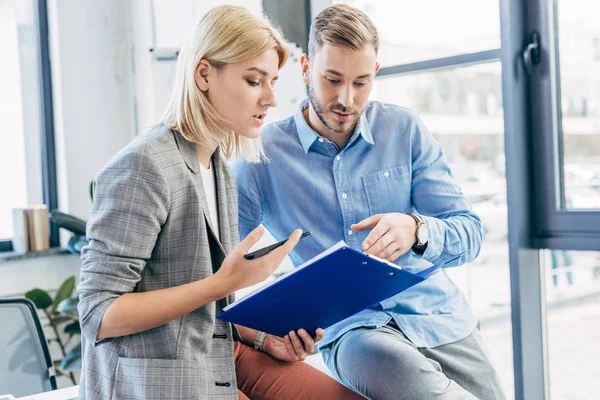 Young business colleagues holding folder and working with papers in office — Stock Photo