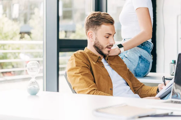 Recortado disparo de guapo joven hombre y mujer coqueteando mientras trabajan juntos en la oficina - foto de stock