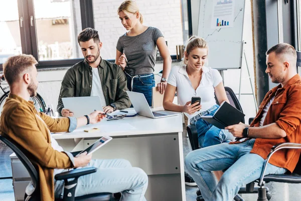 Groupe de jeunes gens d'affaires occasionnels travaillant avec des gadgets ensemble au bureau — Photo de stock